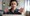 A woman with a headset on and expressive hands having a video call on her laptop