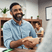 A seated bearded man is a work environment is shaking hands with another man who is mainly out of shot