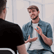 A young bearded bearded man talking to a colleague who has his back to us