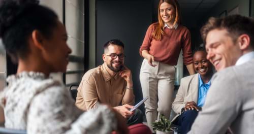 A group of 5 work colleagues sitting on comfortable chairs around a low table having a friendly chat.