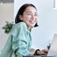 Young woman at her desk on her laptop looking at some one in the room and smiling